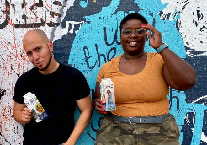 Two people standing against a wall holding cartons of FreeWater.