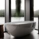 A white free-standing bathtub in a room of glass walls, with a green plant hanging overhead.