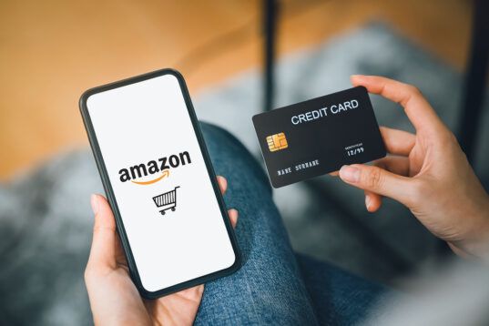 person holding phone shopping on Amazon in one hand and a credit card in the other hand