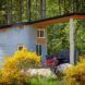 A curved concrete home with an overhang that covers a small outdoor patio with chairs and a table. Greenery surrounds the home.