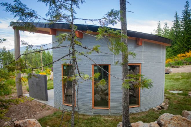 The back of a curved concrete home with an overhang and three narrow windows.