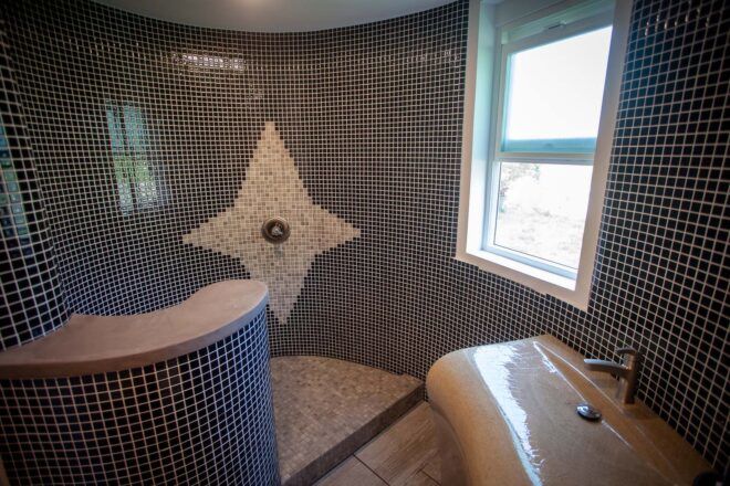 A black tile bathroom with a white tile star design near the faucet.