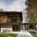 A two-story home with the top floor featuring wood siding. A third, box-like structure is attached to the lower story. A pool and patio sit in the backyard.