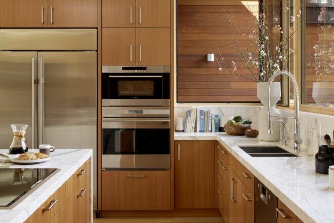 A kitchen with wood cabinets, white marble counters and stainless steel appliances built in to the cabinets.