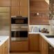 A kitchen with wood cabinets, white marble counters and stainless steel appliances built in to the cabinets.