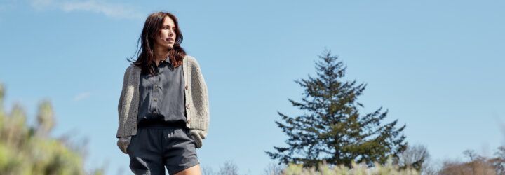 A person wearing a shirt, cardigan and shorts stands on the left, looking off into nature.