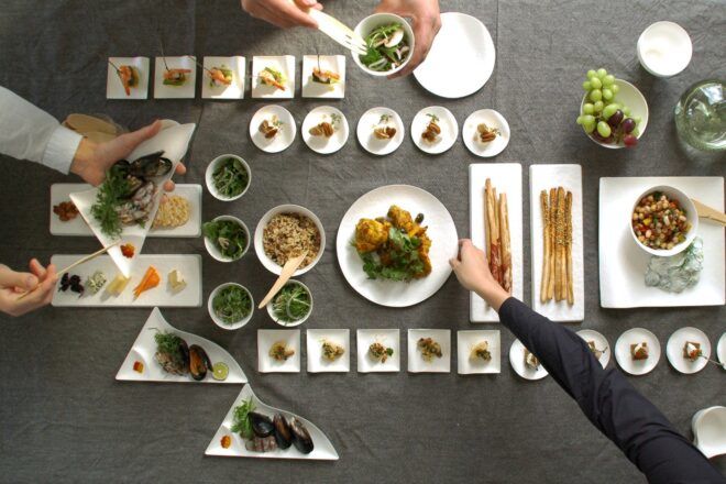 Two hands reaching for plates on either side of a table set with several plates of food.