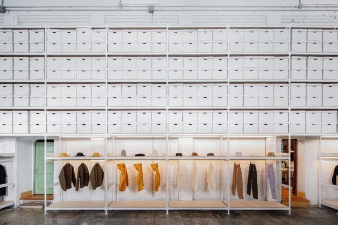 A wall of white cabinets and drawers about a row of clothing racks.
