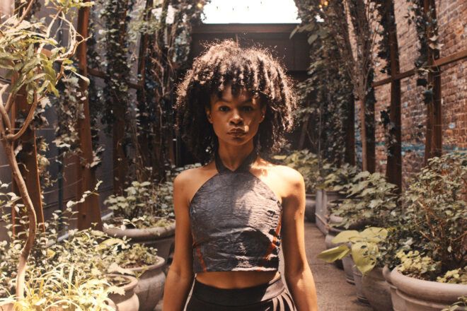 A person in a halter top, standing in a room full of plants.