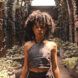 A person in a halter top, standing in a room full of plants.