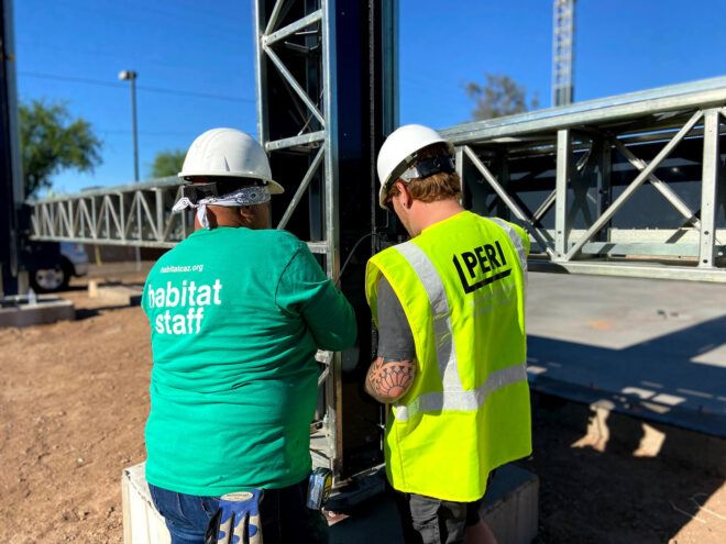 person in Habitat for Humanity shirt and person in PERI Group shirt working together on construction site
