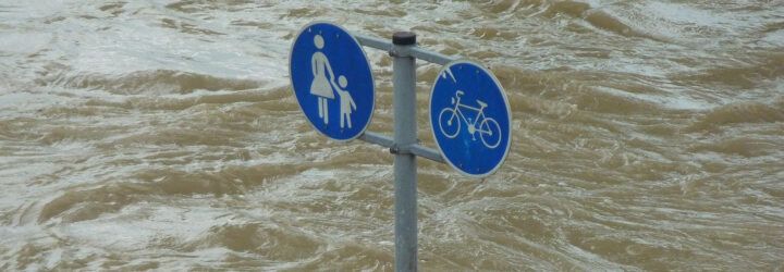 A circular blue road sign being swallowed up by flood water.