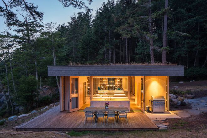 wood home with grassy roof lit from within at night