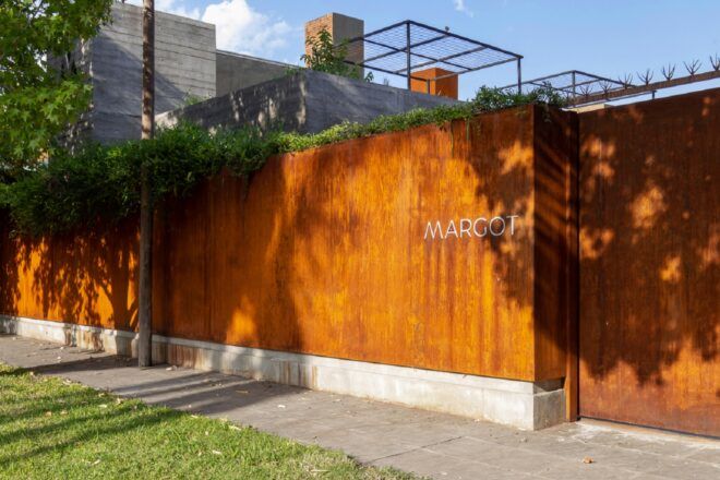 A one-story rectangular volume with letters reading "Margot." A green terrace is partially visible from the roof.