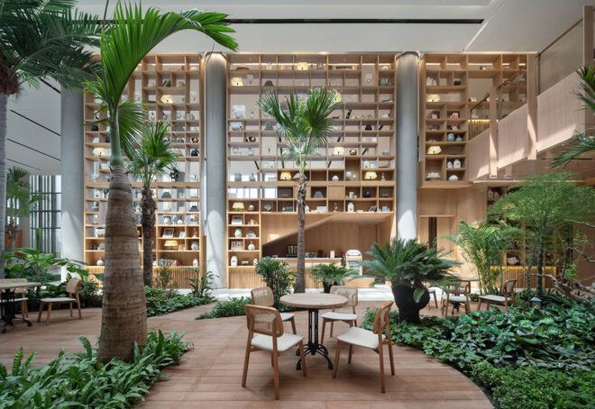 A dining table in the middle of an indoor rainforest area, with large, built-in wooden shelves on the parallel wall.