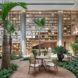 A dining table in the middle of an indoor rainforest area, with large, built-in wooden shelves on the parallel wall.
