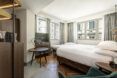 A bedroom with a white bed, white walls and several windows.