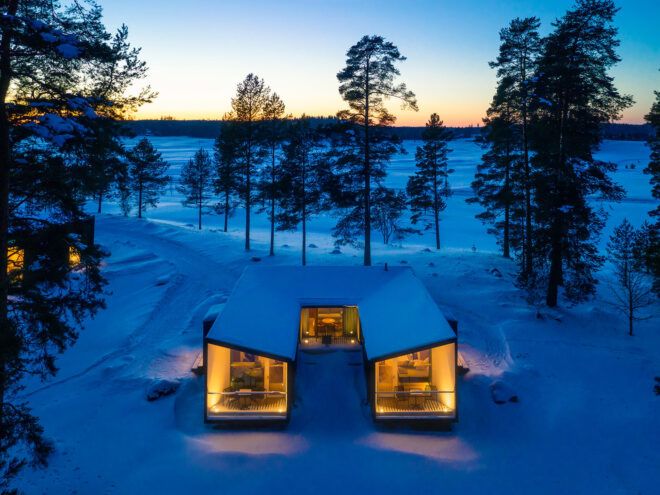 U-shaped cabin covered in snow and lit from within at dusk