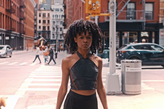 A person in a halter top, standing on the corner of a city street.