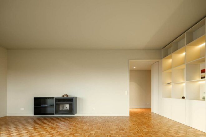 A room with wood floors and white walls with a dark gray cabinet built into one wall and white cabinets to the right.