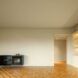 A room with wood floors and white walls with a dark gray cabinet built into one wall and white cabinets to the right.