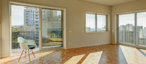 A living room with wood flooring and off-white walls punctuated by large sliding glass doors and windows.