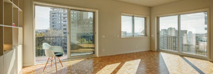 A living room with wood flooring and off-white walls punctuated by large sliding glass doors and windows.