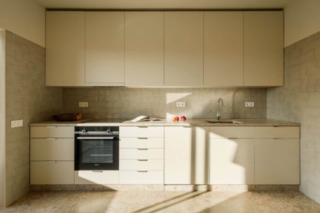 A kitchen with off-white flooring and tile backsplash. The kitchen has white cabinets and a black oven.