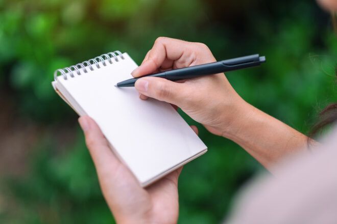 person standing in garden and writing in a notebook