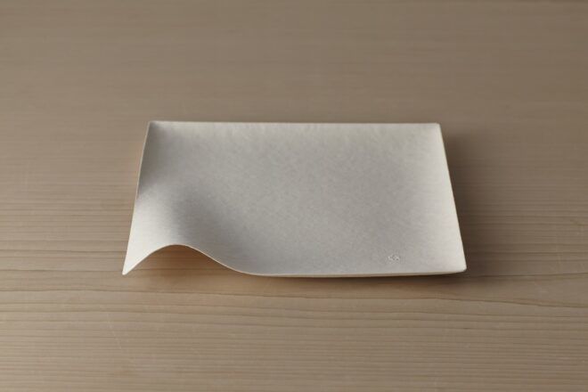 A square plate with a curved lip on the front left corner.