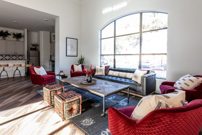 A living room with four red chairs, a coffee table with two cloth blocks to sit on, a gray sofa and a large window behind the sofa.