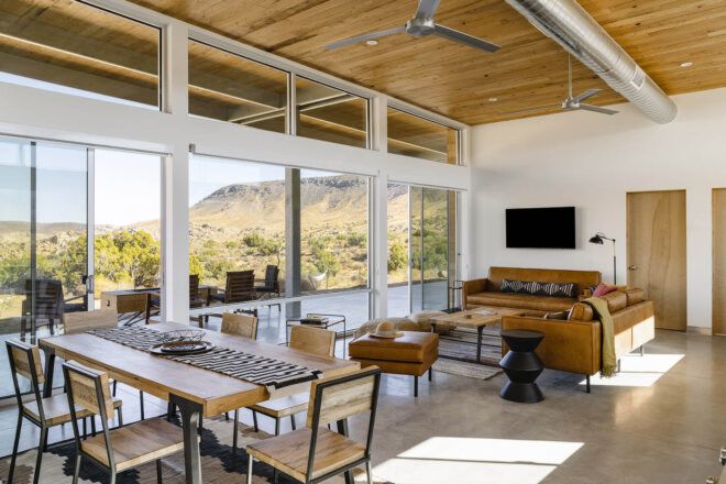 A dining area with a rectangular wood table and chairs connects to a living area with a wall-mounted TV.