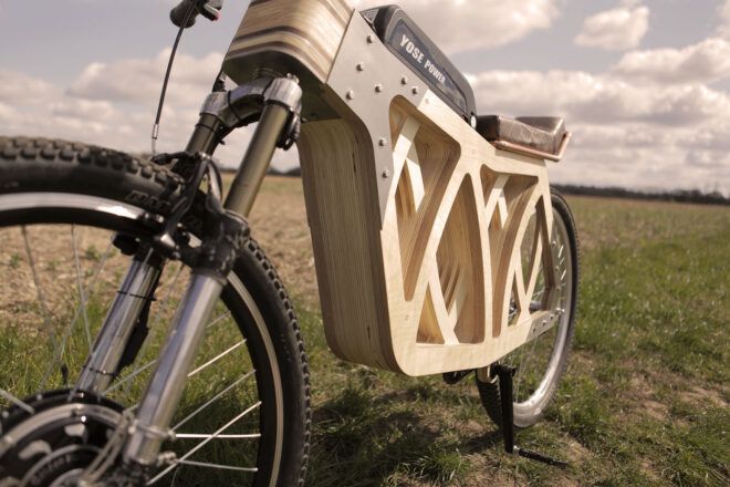 The undercarriage of a wooden e-bike on a grassy lawn.