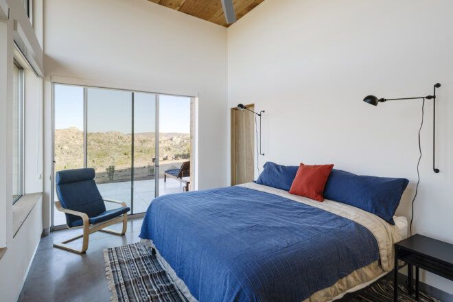A bedroom with sliding glass doors and a bed with a blue comforter, two blue pillows and one red pillow.