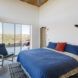 A bedroom with sliding glass doors and a bed with a blue comforter, two blue pillows and one red pillow.