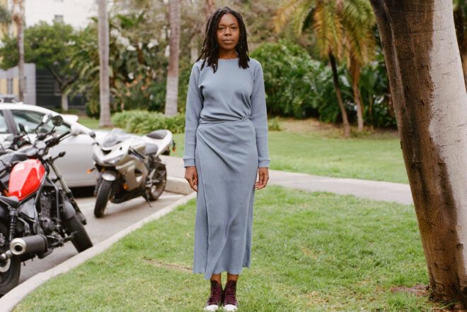 A person standing on grass and wearing a gray calf-length dress.