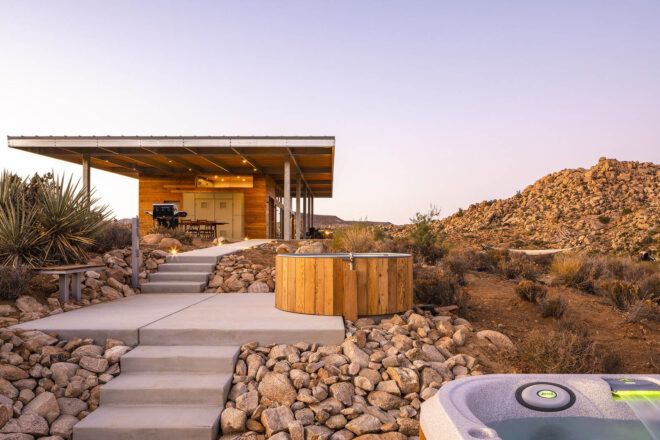 A cement walkway surrounded by stone leads up to a single-level home with a wood facade.