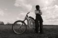 A black-and-white photo of a person in a bike helmet standing next to a wooden e-bike.