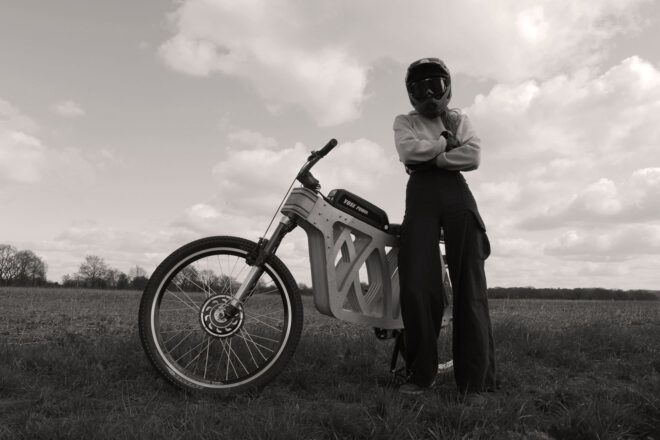 A black-and-white photo of a person in a bike helmet standing next to a wooden e-bike.
