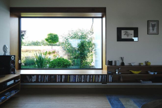 A large rectangular window with a bookshelf underneath looks out onto greenery.