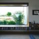 A large rectangular window with a bookshelf underneath looks out onto greenery.