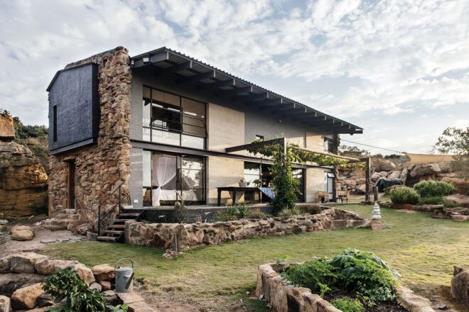 A two-level home with stone accents, large windows and a patio leading to a green lawn.