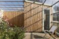 A home with wood cladding and a glass roof cover surrounding a green courtyard.