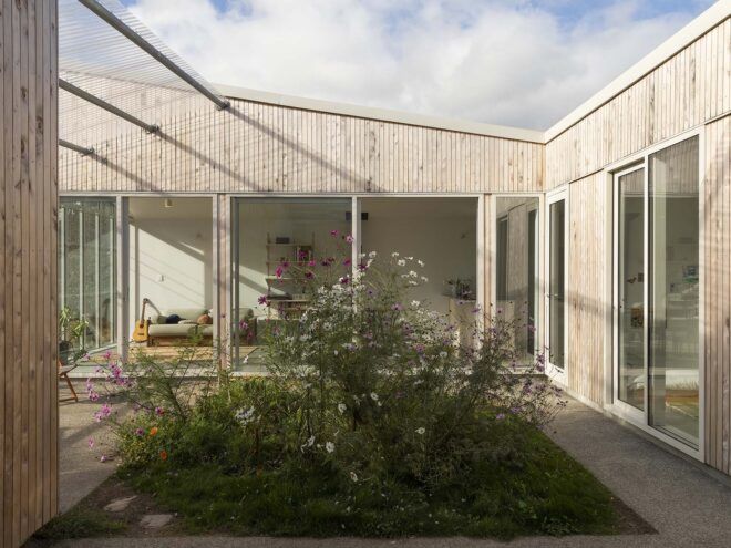 A home with white wood cladding surrounding a green courtyard.