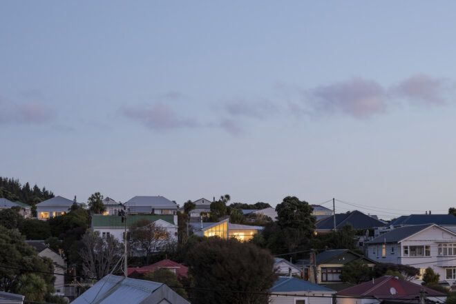 A landscape image of a residential hillside with one home lit up.