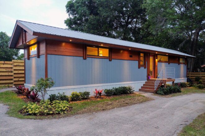 The back of a rectangular tiny home with gray panels covering a portion of the facade, with wood toward the top of the home.