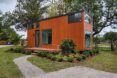 A rectangular tiny home on an elevated porch, with orange-toned wood siding.