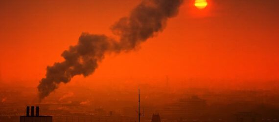 A smokestack emitting smoke against an orange sky.