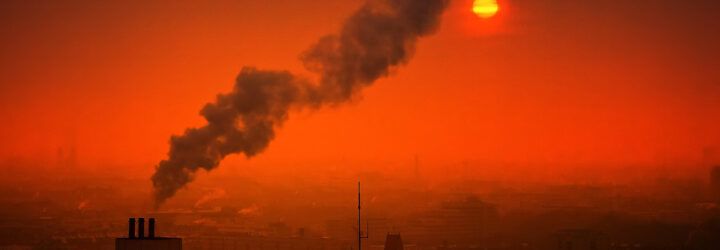 A smokestack emitting smoke against an orange sky.