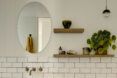 A white bathroom with an oval-shaped mirror and shelves built into the wall.